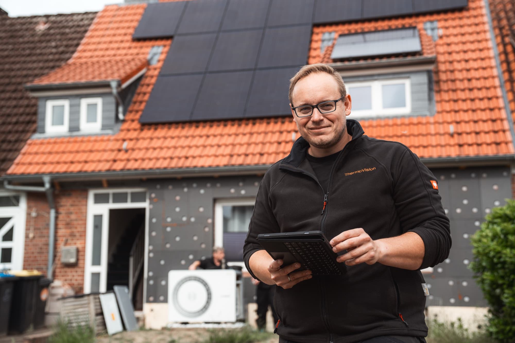ThermoVision Mitarbeiter mit Tablet vor einem Wohnhaus mit Photovoltaikanlage